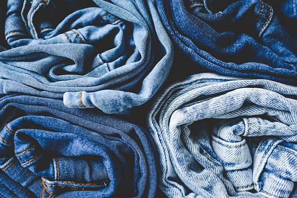 A stack of rolled blue and beige jeans on a neutral background, perfect for minimalist fashion displays or wardrobe organization themes.