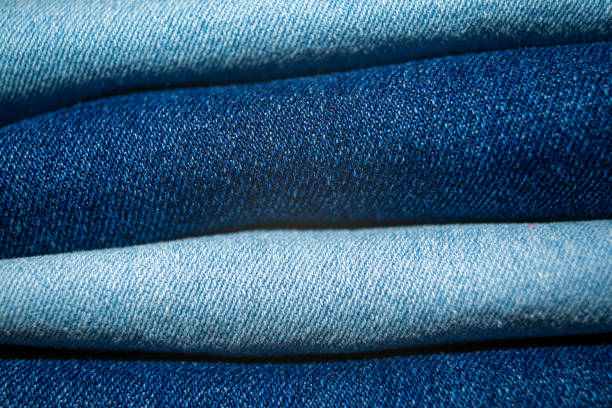 Close up view of folded jeans fabric displaying rich textures and different blue tones, highlighting the fabric's quality and style.