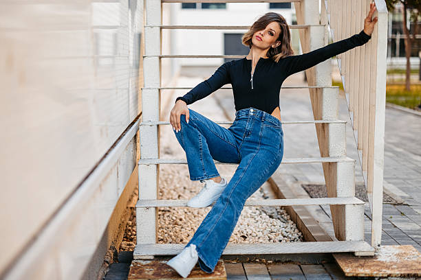 Portrait of a beautiful young woman in jeans and a blouse sitting on the staircase outdoors.