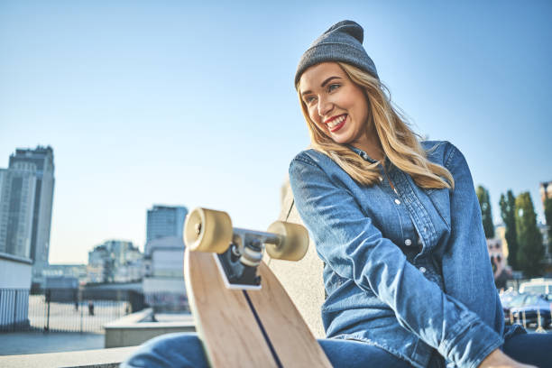 Stylish woman with skateboard sitting on stairs outdoors.